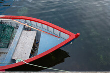 A White Wooden Traditional Dory Or Small Fishing Vessel With Red Trim On A Smooth Water Surface. The Dory Has Wooden Oars And Green Rope.  The Interior Of The Small Vessel Is A Pale Blue Color. 