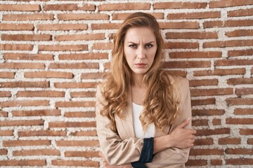 Poster - Beautiful blonde woman standing over bricks wall skeptic and nervous, disapproving expression on face with crossed arms. negative person.