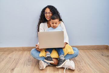 Poster - Young hispanic mother and kid using computer laptop sitting on the floor winking looking at the camera with sexy expression, cheerful and happy face.