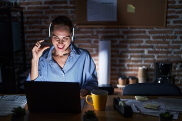 Sticker - Beautiful brunette woman working at the office at night smiling and confident gesturing with hand doing small size sign with fingers looking and the camera. measure concept.