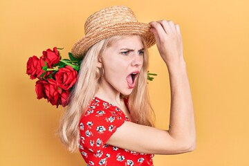 Sticker - Beautiful caucasian woman with blond hair holding bouquet of red roses angry and mad screaming frustrated and furious, shouting with anger. rage and aggressive concept.