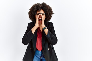 Wall Mural - African american woman with afro hair wearing business jacket and glasses shouting angry out loud with hands over mouth