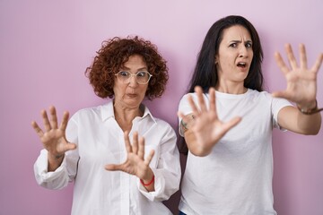 Poster - Hispanic mother and daughter wearing casual white t shirt over pink background afraid and terrified with fear expression stop gesture with hands, shouting in shock. panic concept.