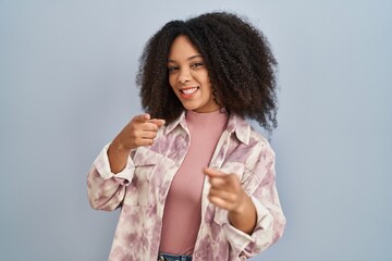 Poster - Young african american woman standing over blue background pointing fingers to camera with happy and funny face. good energy and vibes.