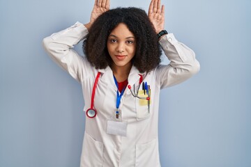 Canvas Print - Young african american woman wearing doctor uniform and stethoscope doing bunny ears gesture with hands palms looking cynical and skeptical. easter rabbit concept.