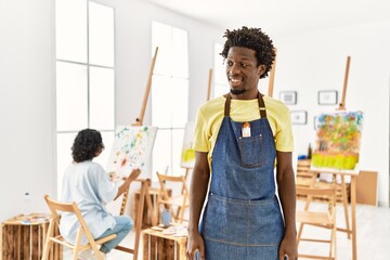 Canvas Print - African young man standing at art studio looking away to side with smile on face, natural expression. laughing confident.