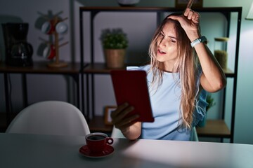 Canvas Print - Young hispanic woman using touchpad sitting on the table at night making fun of people with fingers on forehead doing loser gesture mocking and insulting.