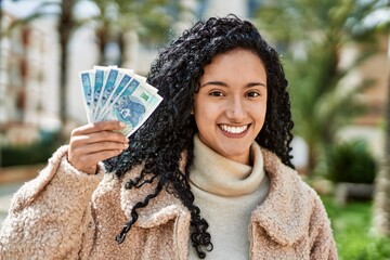 Young hispanic woman smiling confident holding zloty banknotes at park