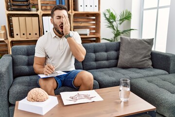 Poster - Handsome hispanic man working with rorschach test at psychology clinic yawning tired covering half face, eye and mouth with hand. face hurts in pain.