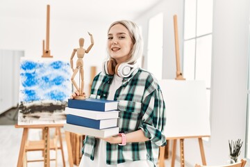 Poster - Young artist student girl smiling happy using headphones and holding books at art studio.