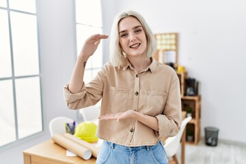 Sticker - Young beautiful caucasian woman at construction office gesturing with hands showing big and large size sign, measure symbol. smiling looking at the camera. measuring concept.