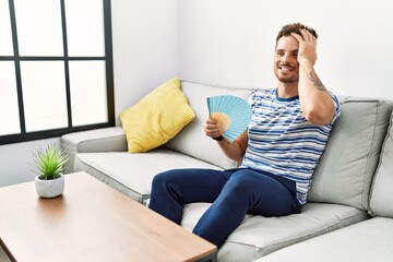 Canvas Print - Young hispanic man smiling confident using hand fan at home