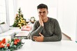 © Krakenimages.com - Young hispanic man sitting on the table by christmas tree touching mouth with hand with painful expression because of toothache or dental illness on teeth. dentist