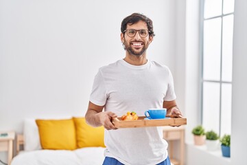 Sticker - Handsome latin man eating breakfast on the bed smiling with a happy and cool smile on face. showing teeth.