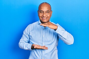 Wall Mural - Middle age latin man wearing casual clothes and glasses gesturing with hands showing big and large size sign, measure symbol. smiling looking at the camera. measuring concept.