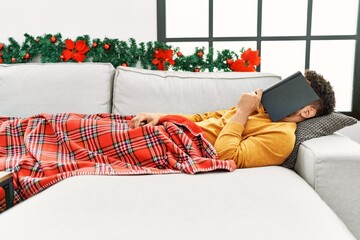 Canvas Print - Young arab man sleeping with book on head lying on the sofa by christmas decor at home.