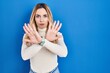 Young caucasian woman standing over blue background rejection expression crossing arms and palms doing negative sign, angry face