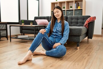 Wall Mural - Young chinese girl smiling happy sitting on the floor at home.