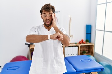 Poster - Young handsome physiotherapist man working at pain recovery clinic looking at the watch time worried, afraid of getting late