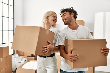 Poster - Young beautiful couple smiling happy holding cardboard boxes at new home.