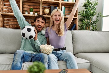 Poster - Young couple watching soccer match eating porpcorn at home.