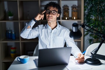 Poster - Hispanic man working at the office at night smiling pointing to head with one finger, great idea or thought, good memory