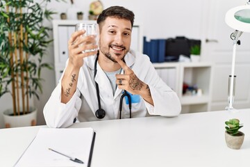 Sticker - Young doctor holding glass of water smiling happy pointing with hand and finger