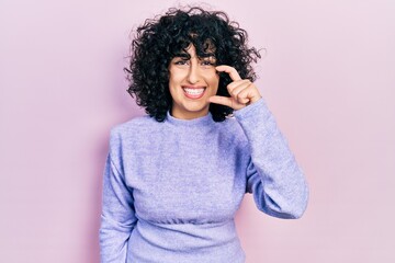 Sticker - Young middle east woman wearing casual clothes smiling and confident gesturing with hand doing small size sign with fingers looking and the camera. measure concept.