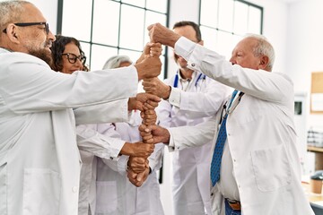 Wall Mural - Group of middle age doctor smiling happy bulding tower with fists in a medical meeting at the clinic office.