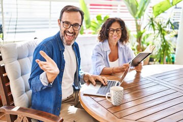 Canvas Print - Middle age couple relaxing at home terrace celebrating achievement with happy smile and winner expression with raised hand