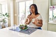 Young hispanic woman eating healthy salad at home disgusted expression, displeased and fearful doing disgust face because aversion reaction. with hands raised