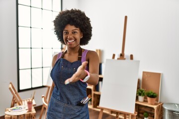 Canvas Print - Young african american woman with afro hair at art studio smiling friendly offering handshake as greeting and welcoming. successful business.