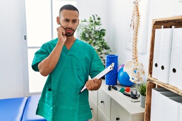 Poster - African american physiotherapist man working at pain recovery clinic touching mouth with hand with painful expression because of toothache or dental illness on teeth. dentist concept.