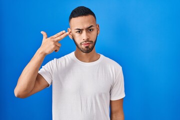 Poster - Young hispanic man standing over blue background shooting and killing oneself pointing hand and fingers to head like gun, suicide gesture.