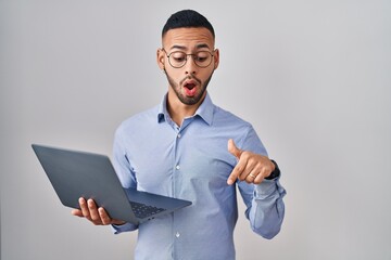 Poster - Young hispanic man working using computer laptop pointing down with fingers showing advertisement, surprised face and open mouth