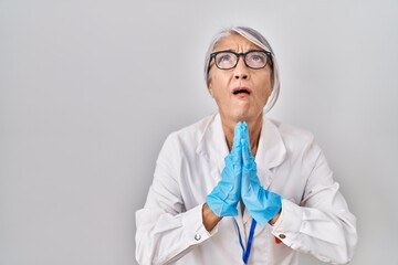 Poster - Middle age woman with grey hair wearing scientist robe begging and praying with hands together with hope expression on face very emotional and worried. begging.