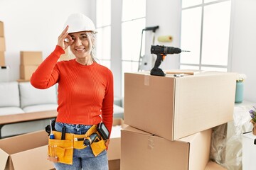 Poster - Middle age grey-haired woman wearing hardhat standing at new home doing ok gesture with hand smiling, eye looking through fingers with happy face.