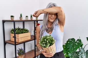 Sticker - Middle age grey-haired woman holding green plant pot at home smiling cheerful playing peek a boo with hands showing face. surprised and exited