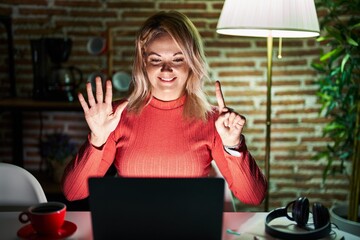 Canvas Print - Blonde woman using laptop at night at home showing and pointing up with fingers number six while smiling confident and happy.