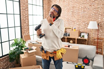 Canvas Print - Handsome middle age man holding screwdriver at new home with hand on chin thinking about question, pensive expression. smiling with thoughtful face. doubt concept.