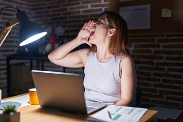 Poster - Brunette woman working at the office at night shouting and screaming loud to side with hand on mouth. communication concept.