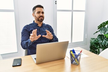 Poster - Young hispanic man with beard working at the office with laptop disgusted expression, displeased and fearful doing disgust face because aversion reaction.