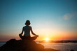 © De Visu - A woman does yoga, meditating on an ocean beach during a beautiful sunset.