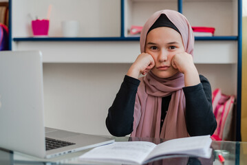 A sad and bored Muslim student girl while learning for school at home desk.