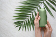 Female hands with cosmetic product and tropical leaf on light background