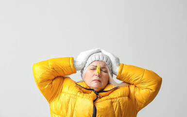 Poster - Ill mature woman with clothespin on light background. Stuffy nose concept