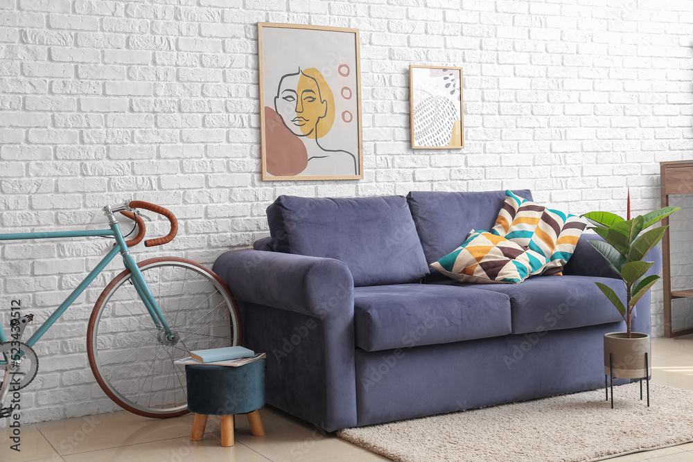Bicycle, blue sofa, pouf and houseplant near white brick wall