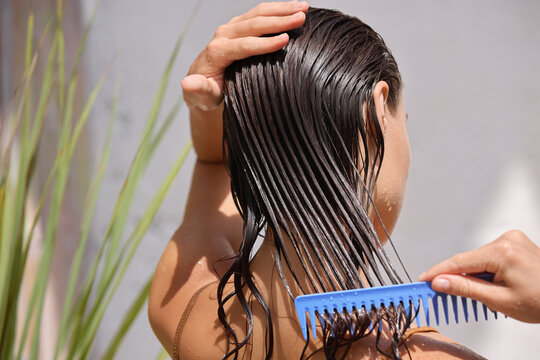 young female model putting refreshing mask on long wet hair with wooden comb. closeup of beautiful w