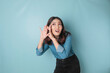 © Reezky - Amazed curious bride young woman wearing a blue shirt trying to hear you overhear listening intently isolated on blue turquoise background studio portrait.