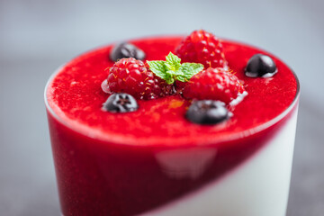 Panna cotta dessert with sauce from berries. Cherries, raspberries and blueberry as decoration. Served in two glasses on dark background. Traditional Italian creamy dessert.